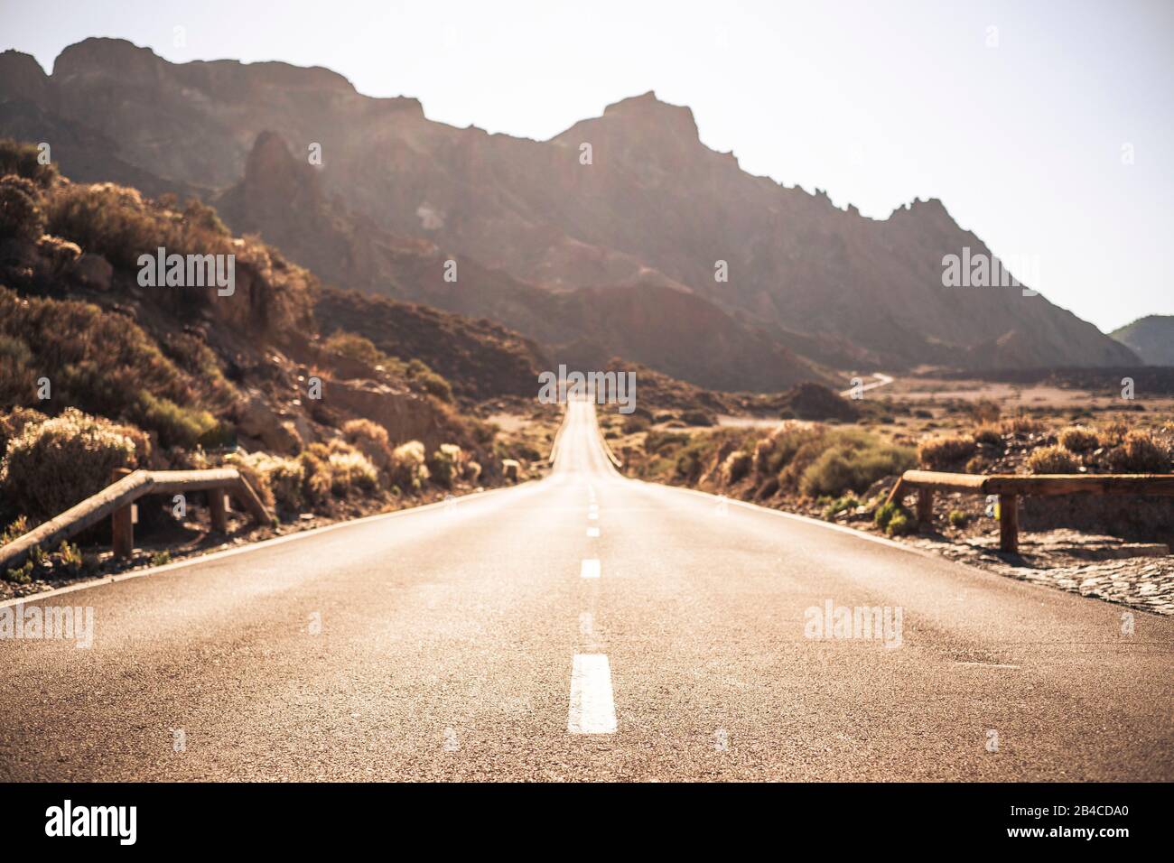 Beautiful and scenic long way road with focus on foreground - defocused background and travel destination effect with sunilght and mountains Stock Photo