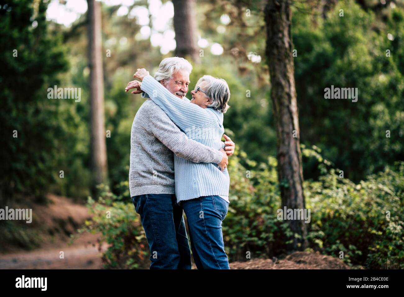 Senior active couple enjoying the outdoor nature forest with hugs and love together - forever life concept with mature man and woman - elderly and beautiful forest green in background Stock Photo