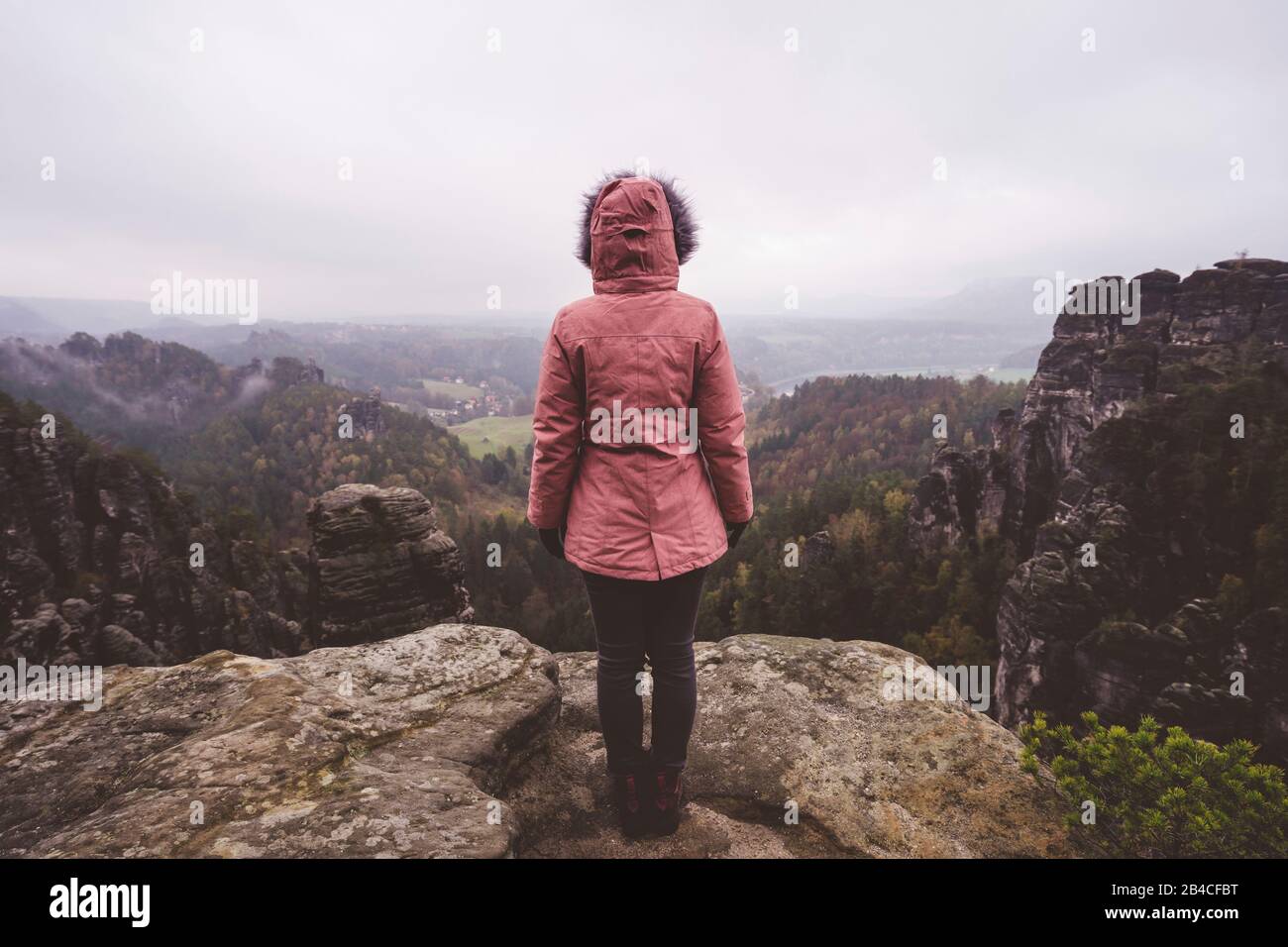 Junge Frau in winterlicher Kleidung im Freien, die allein auf einem Berg steht und die Aussicht genießt, Reiselebensstil-Harmoniekonzept, Rückansicht Stock Photo