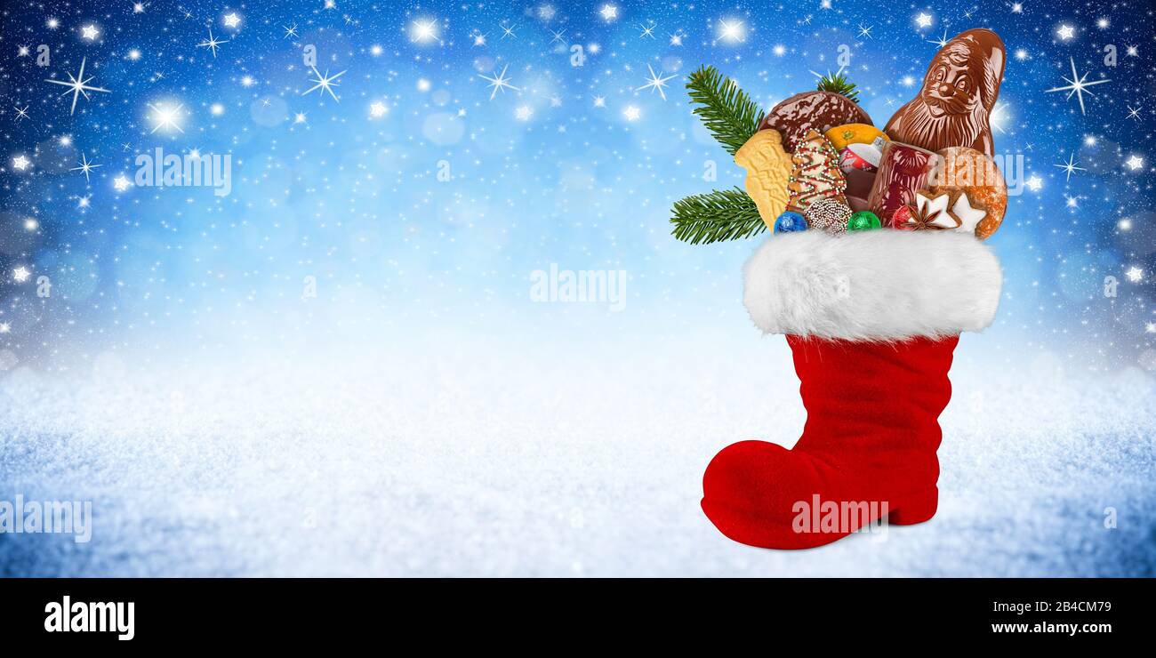 Red st nicholas day boot filled with chocolate santa claus cookies gingerbread cinnamon stars orange and green fresh fir branches on blue white snow p Stock Photo