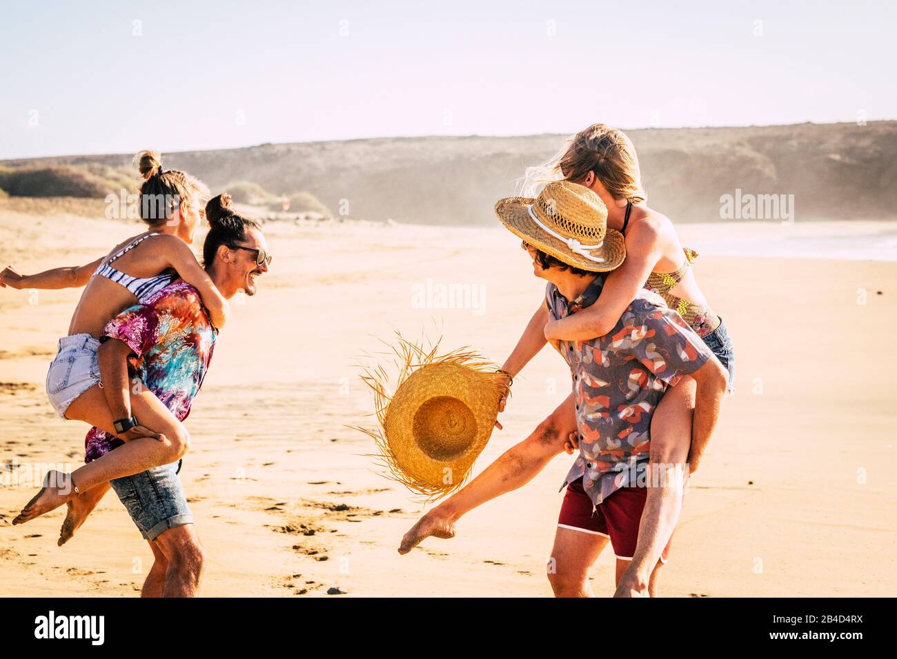 Group of happy and cheerful young people enjoying the outdoor leisure activity during hoilday summer vacation playing at the beach - boys carrying girls and have fun together Stock Photo