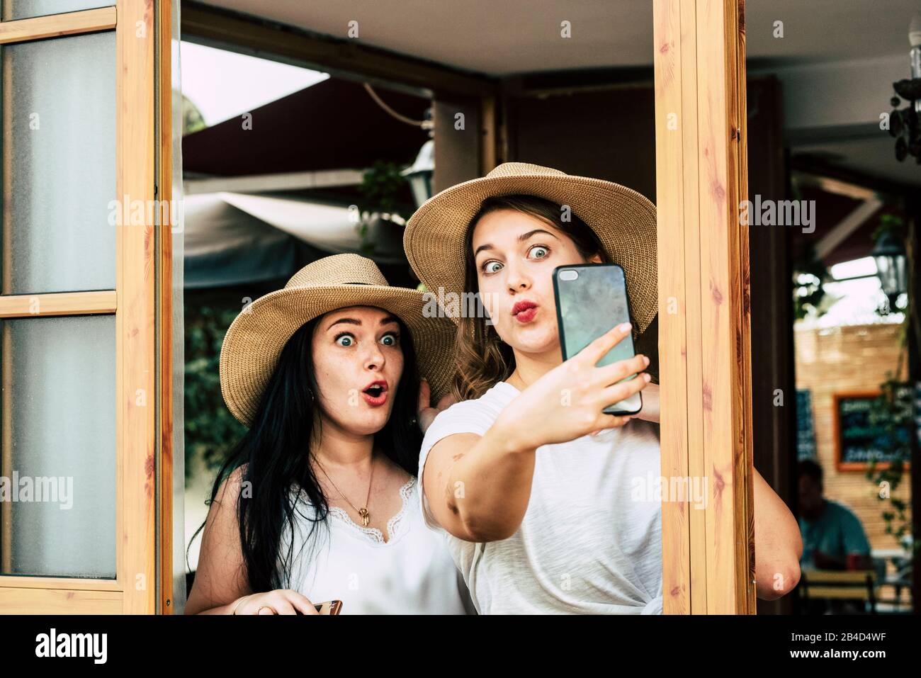 Couple of young caucasian women friends have fun taking selfie pictures together with funny expressions - people enjoying with technology phone device in oudoor Stock Photo