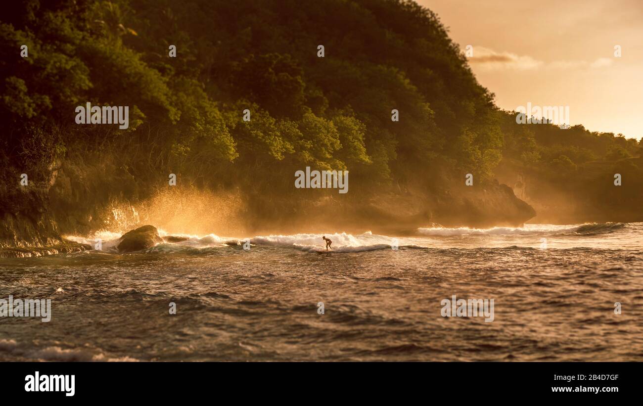 Local Kids surf on Waves in Sunset light, Beautiful Crystal Bay, Nusa Penida, Bali Stock Photo