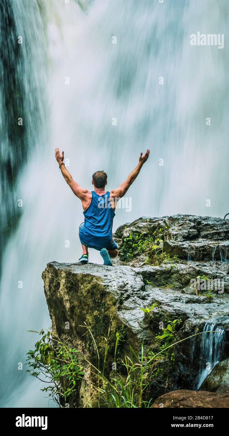 Man sitting in Front of Tegenungan Waterfall near Ubud raising hands and rhapsodize it, Bali, Indonesia. Stock Photo