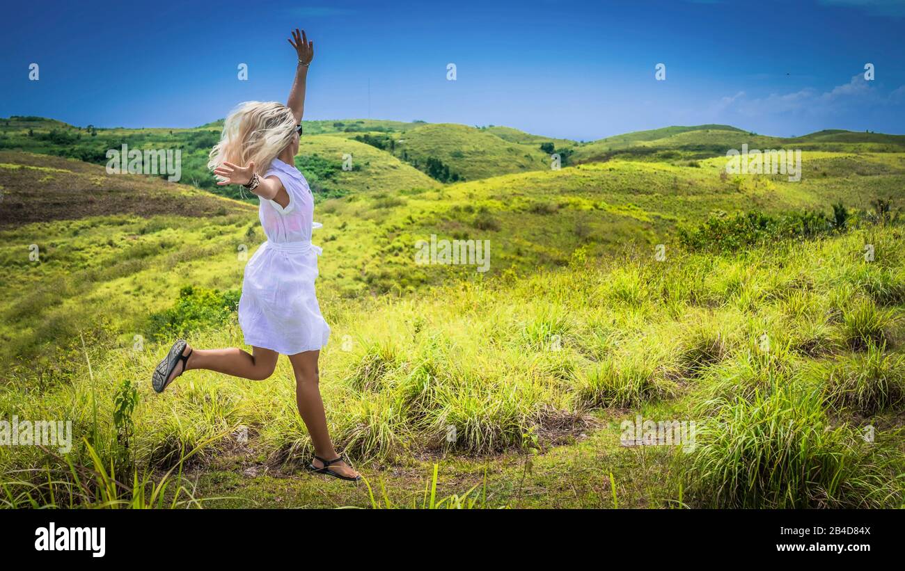 A girl in white dress happy jumping on green grass Hill, Teletubbies Hills, Nusa Penida, Bali, Indonesia. Stock Photo