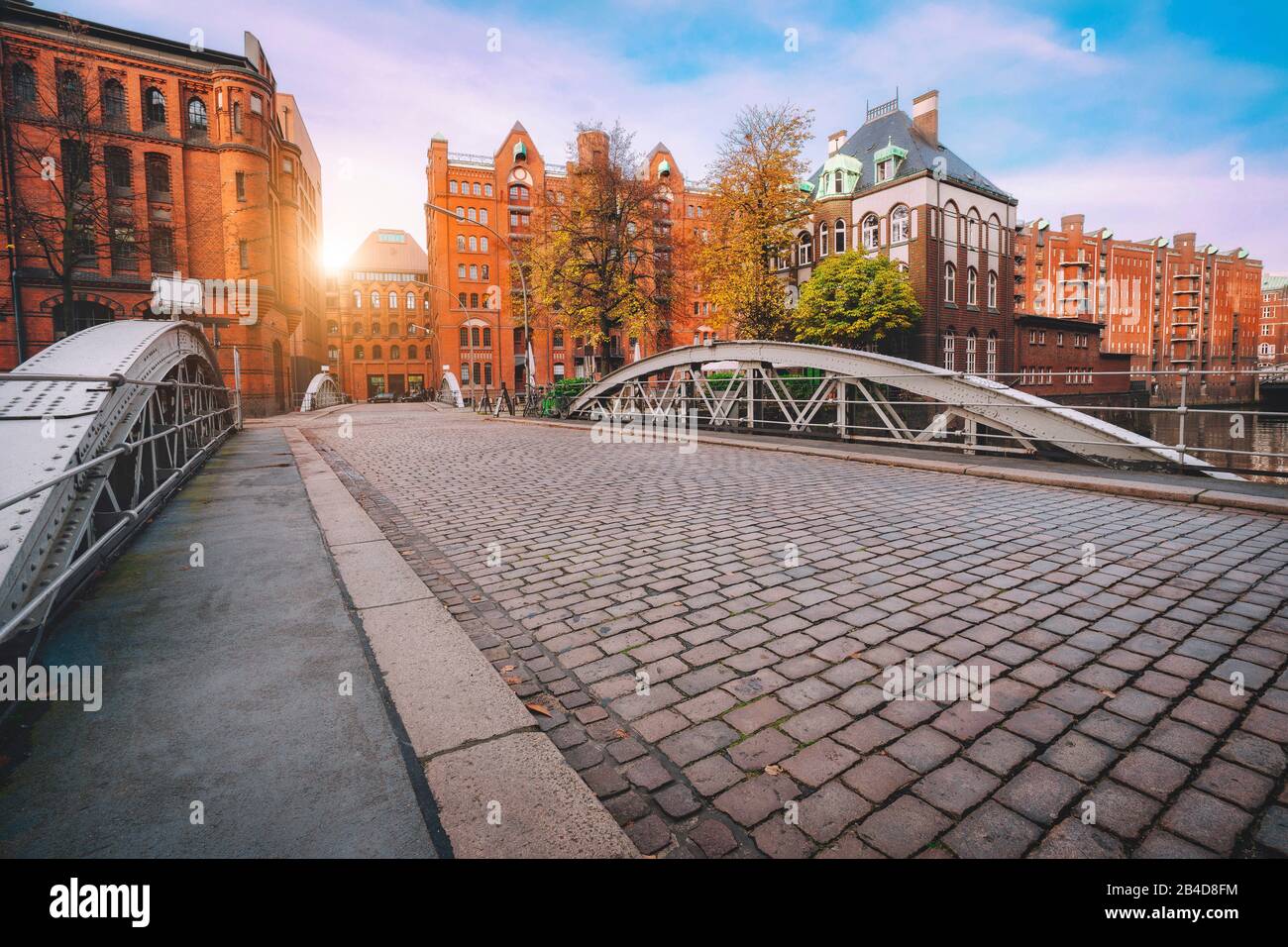 Arch bridge over canals with cobbled street in the warehouse district of Hamburg, Germany, Europe, historic brick building illuminated by golden sunset Stock Photo
