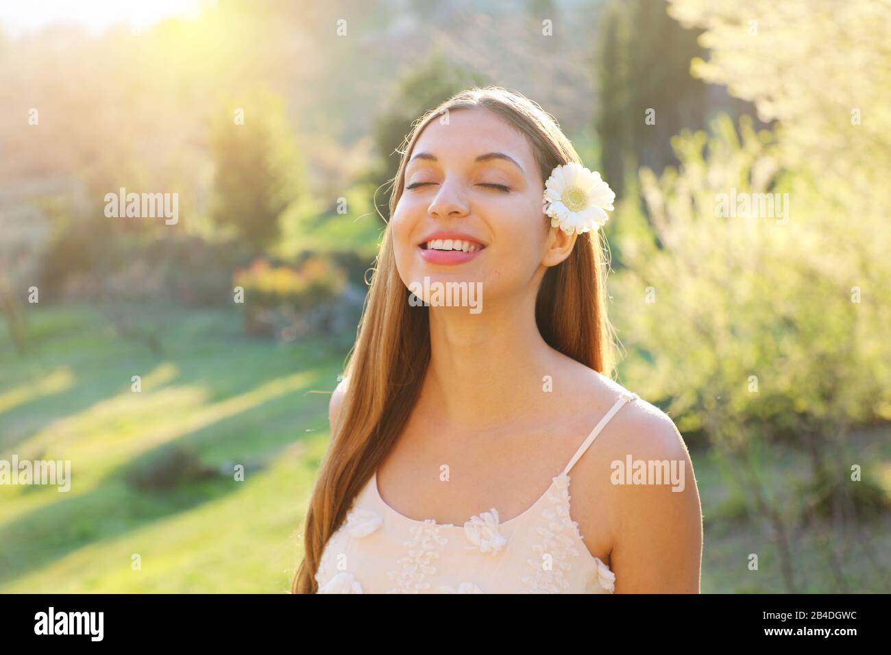Pretty beautiful girl with closed eyes and flower on ear smiling enjoying breathing fresh air outdoor Stock Photo