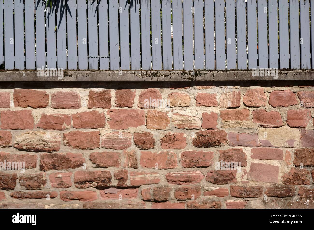 A rustic wall of staggered and broken bricks with a wooden fence. Stock Photo