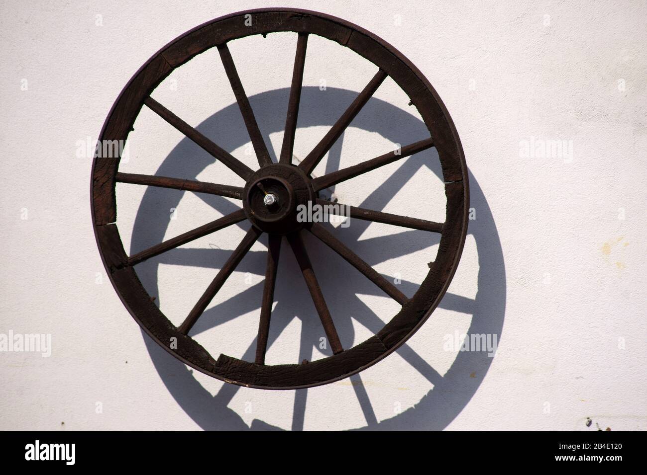 An old, nostalgic spoked wheel of a coach or a trailer hangs on the wall of a farmhouse for decorative purposes. Stock Photo
