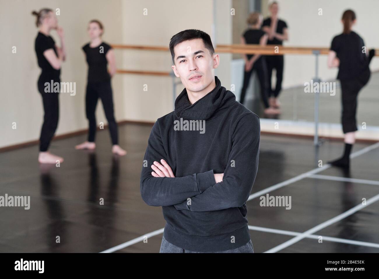 Young confident instructor of modern ballet dancing course crossing arms by chest while standing in front of camera in studio Stock Photo