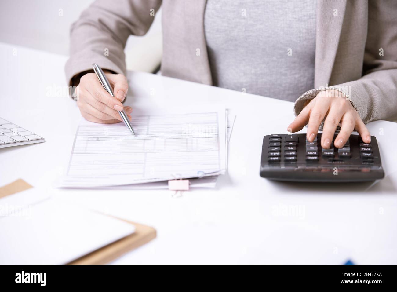Hands of young elegant accountant with pen over financial document pressing buttons of calculator while working by desk Stock Photo