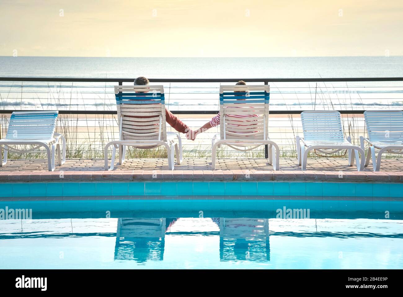 USA, Folrida, Daytona Beach, couple in beach chairs by the pool, holding hands, overlooking the sea Stock Photo