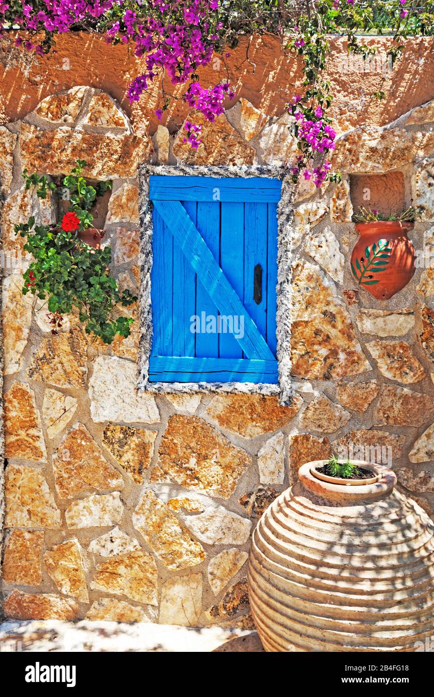 Colorful shutters and doors in stone house decorated with flower tubs, Greece Stock Photo