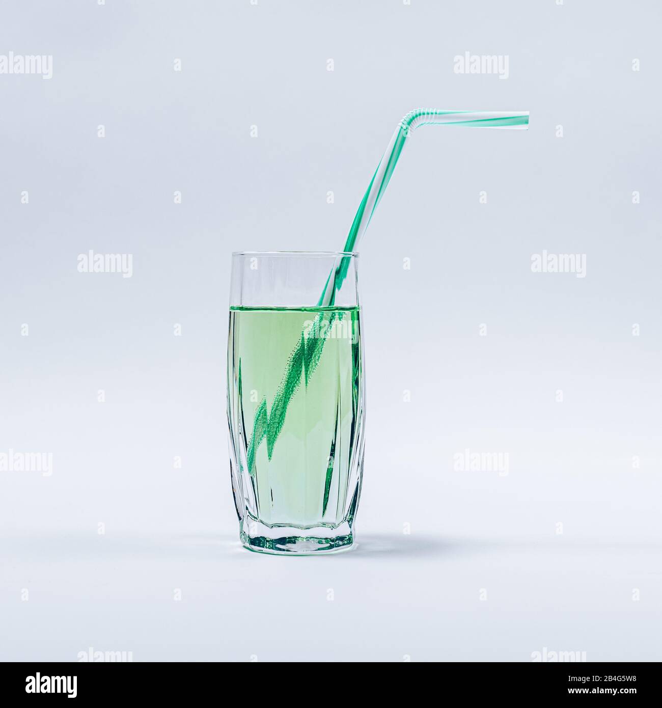 Glass filled with green refreshing drink completed with straw standing in center on white background. Stock Photo