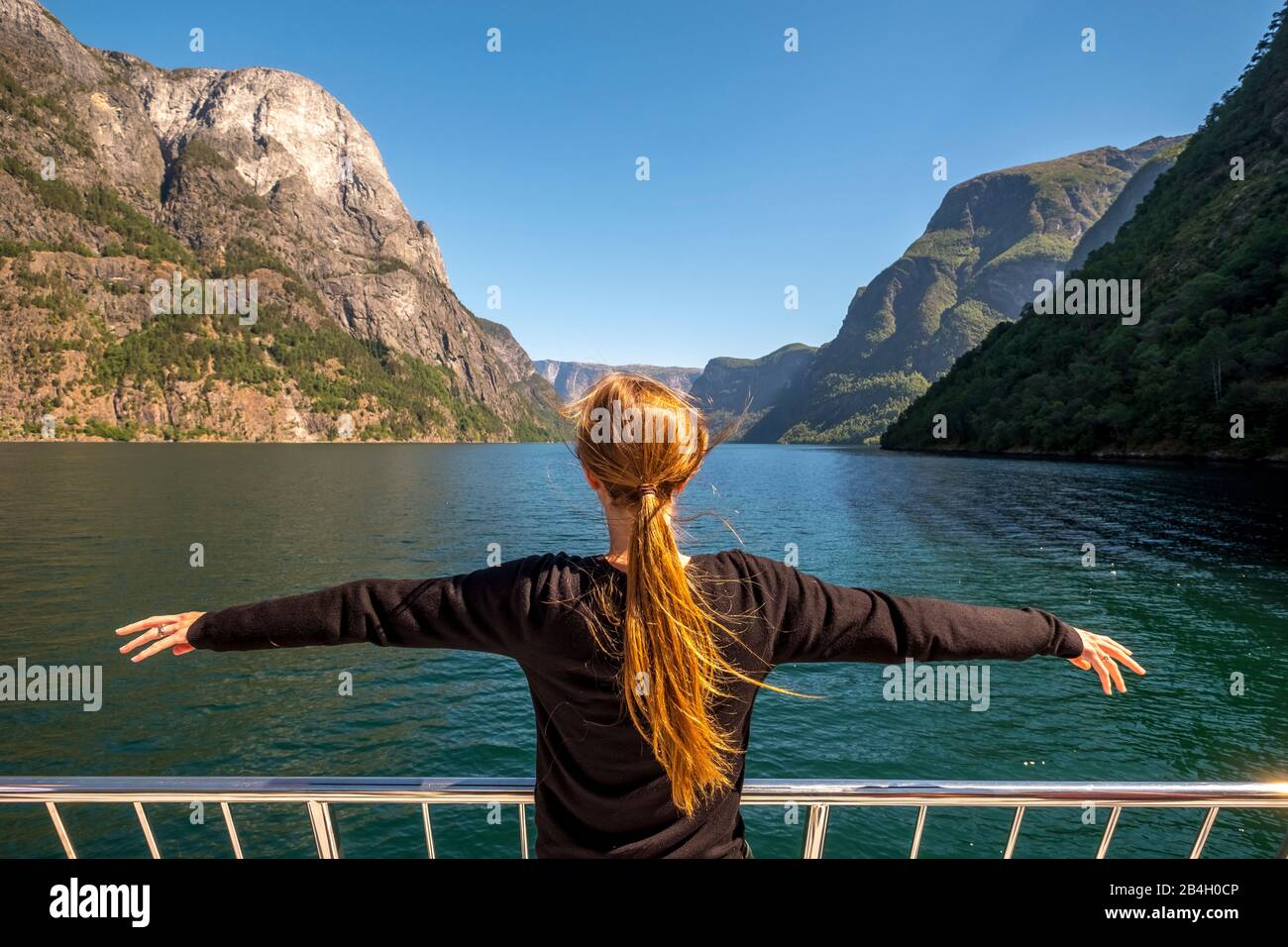 Woman with outstretched arms on excursion ship, fjord, Nærøyfjorden, blue sky, mountains, rock walls, trees, Styvi, Sogn og Fjordane, Norway, Scandinavia, Europe Stock Photo
