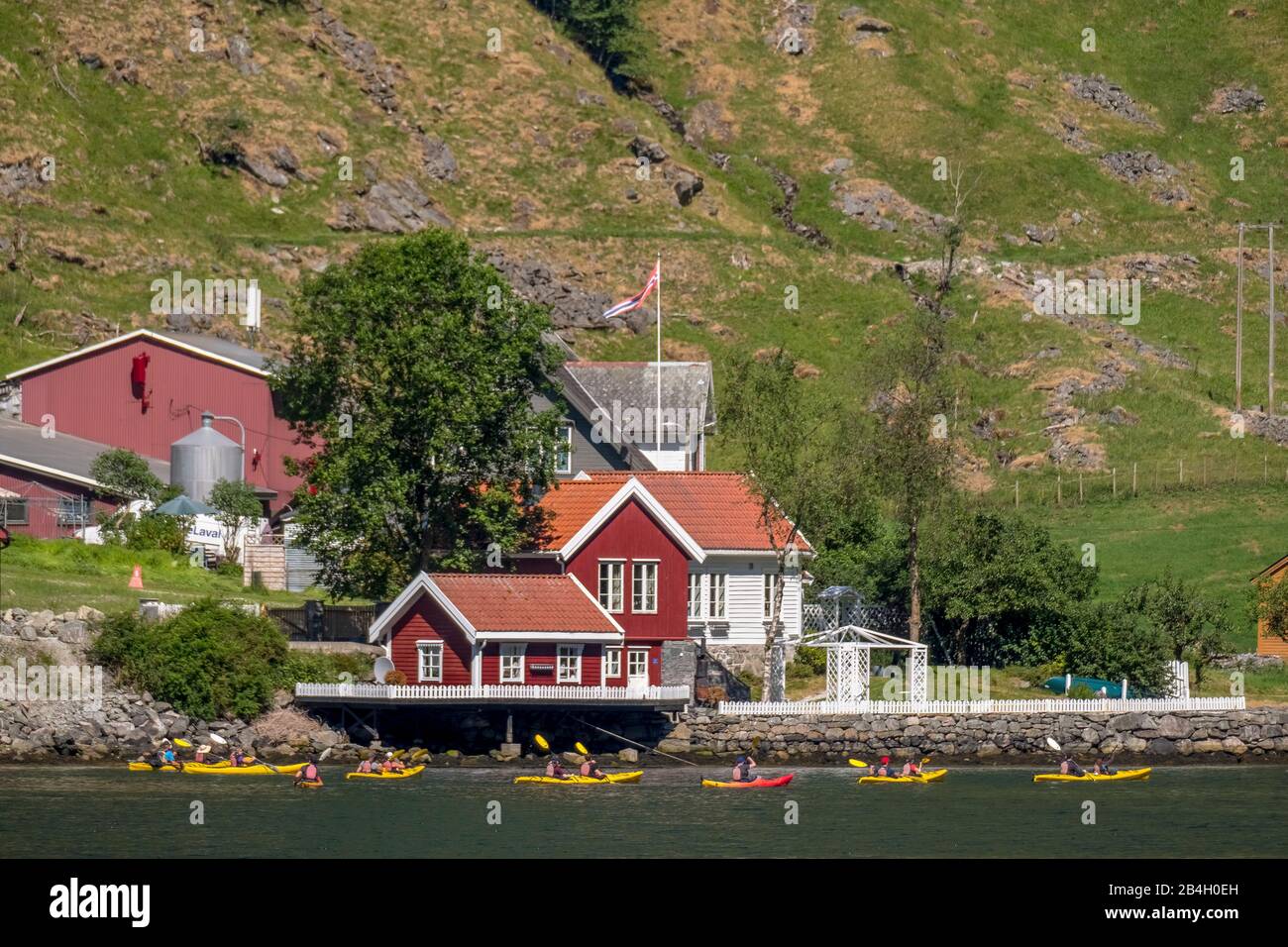 Tourists in yellow kayaks on fjord, Flåm, Gudvangen, stone wall, mountain landscape, red wooden houses, Bakka, Sogn og Fjordane, Norway, Scandinavia, Europe Stock Photo
