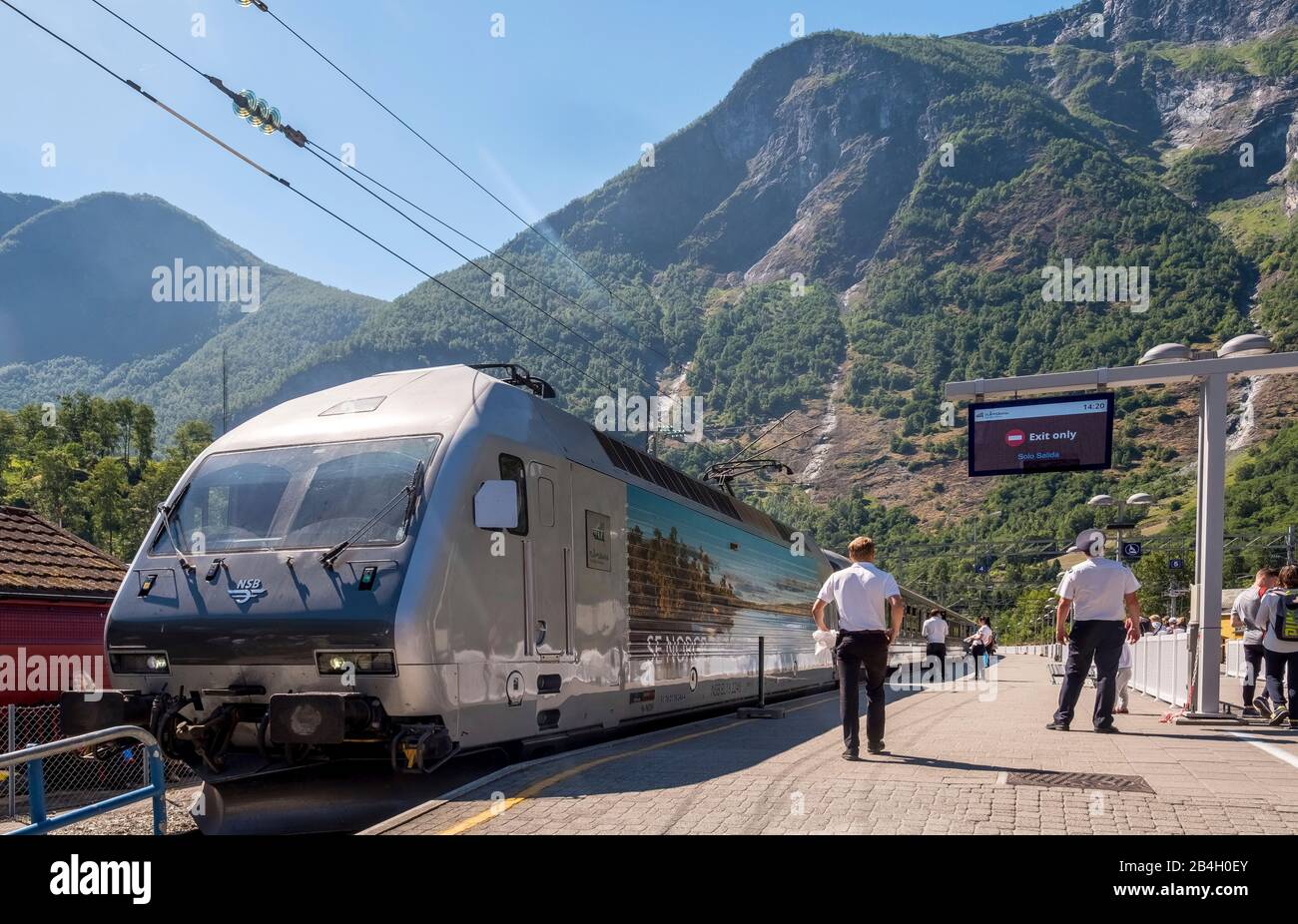 Journey with the Flambahn, Eisenbahreise, people at the railroad track, train NSB, paved stop with scoreboard, mountains, forests, Flåm, Sogn og Fjordane, Norway, Scandinavia, Europe Stock Photo