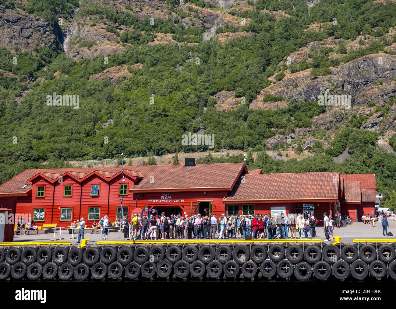 Flåm, tourists at the TICKETS & VISITOR CENTER, red wooden house, pier for ships, rock faces, trees, Sogn og Fjordane, Norway, Scandinavia, Europe Stock Photo