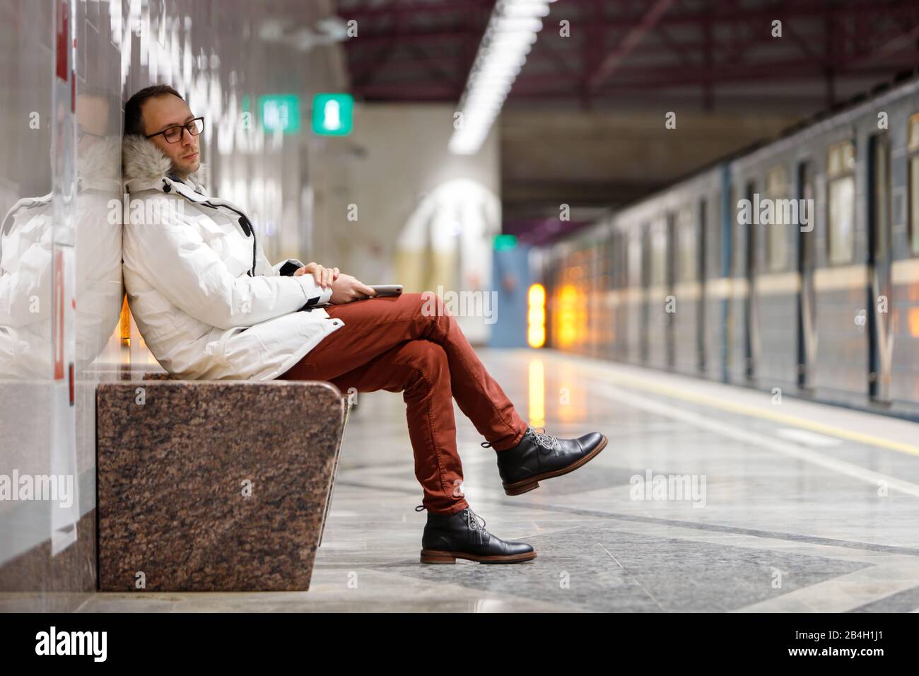 Crying man with feels unhappy and depressed, looking down, receiving bad message, holding smartphone,  on empty subway station. Emotional crisis, trou Stock Photo