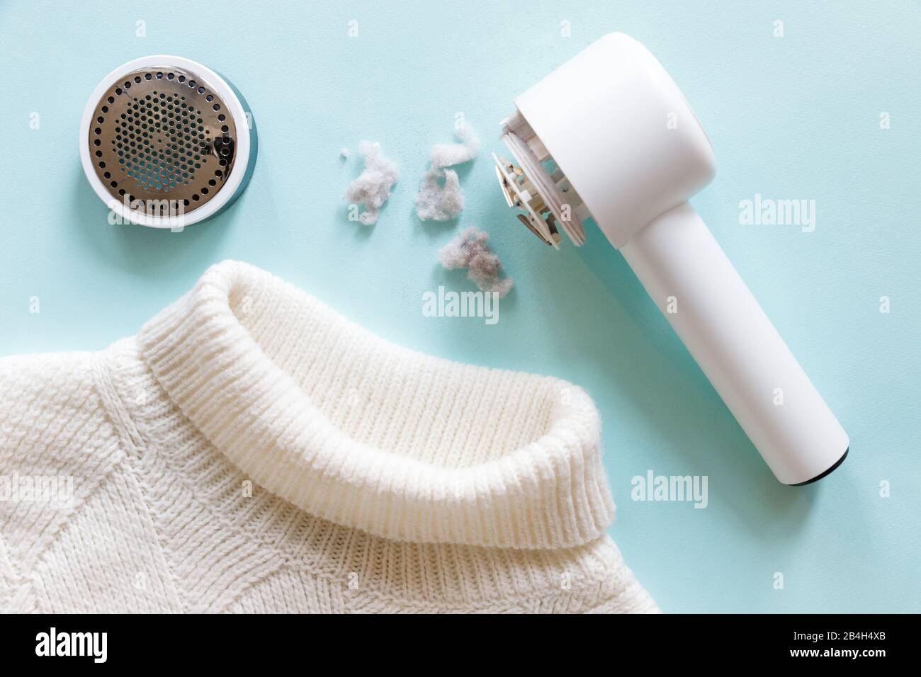 Pilling/ Removing lint from a white acrylic or wool sweater. Electric device after cleaning and collected fluff/lint on light blue background. Top vie Stock Photo