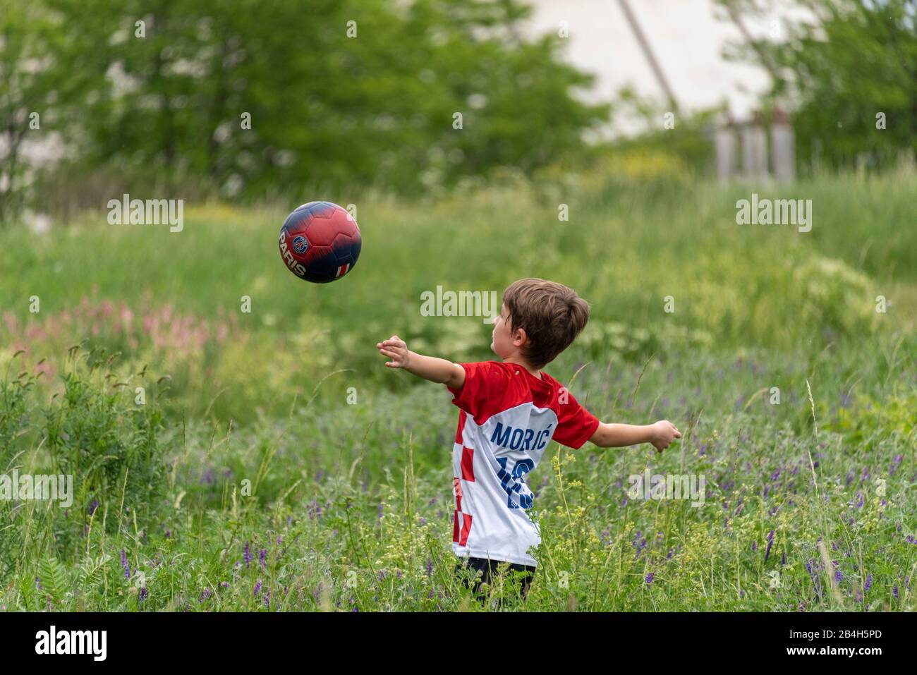 An eight-year-old boy plays soccer in the tall grass, wearing a T-shirt by Croatian footballer Luka Modric Stock Photo