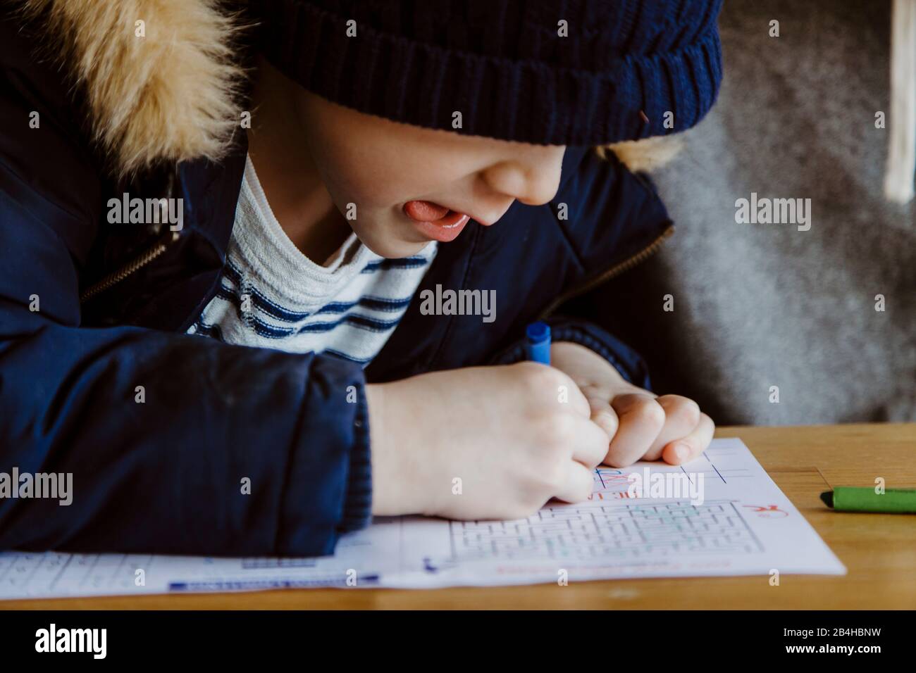 Boy coloring at restaurant table while waiting sticking tongue out Stock Photo