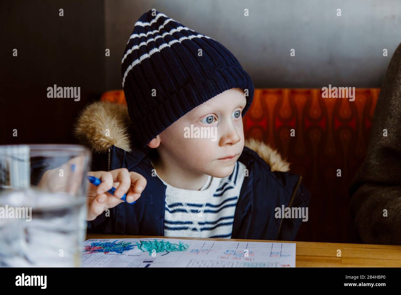 Boy colouring in red restaurant booth wearing white and navy waiting Stock Photo