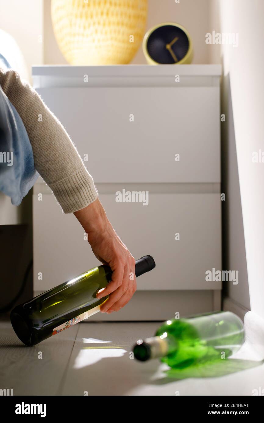 Closeup of alcoholic man fell asleep with a bottle in his hand on bed after party, empty wine bottles on the floor. Alcohol abuse, drunkenness, hangov Stock Photo