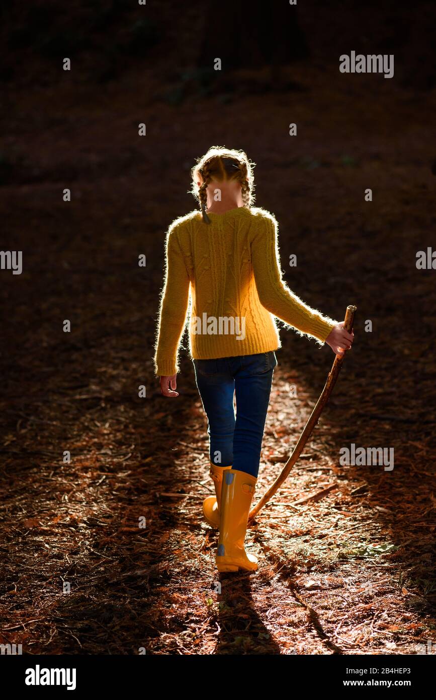 Tween girl with walking stick in forest with beautiful light Stock Photo
