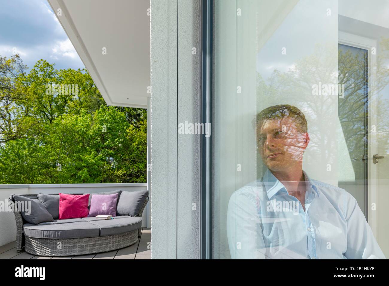 junger Mann blickt durch Glasscheibe in den Außenraum, moderne Architektur Stock Photo