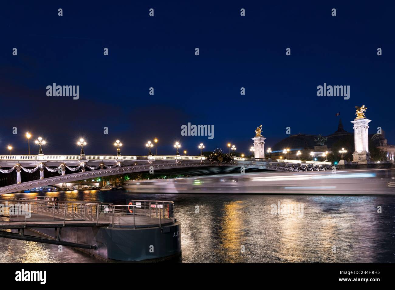 die nachts erleuchtende Brücke Pont Alexandre III unter der ein Ausflusschiff hindurch fährt und eine Lichtspur hinterläßt, Paris, Frankreich, Europa Stock Photo