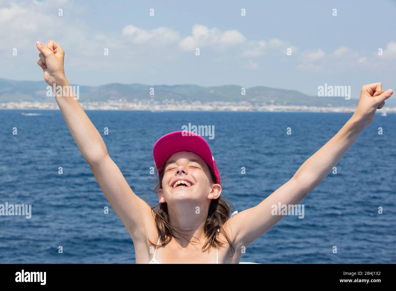 Girl with a cap by the sea, joy, arms up, portrait Stock Photo