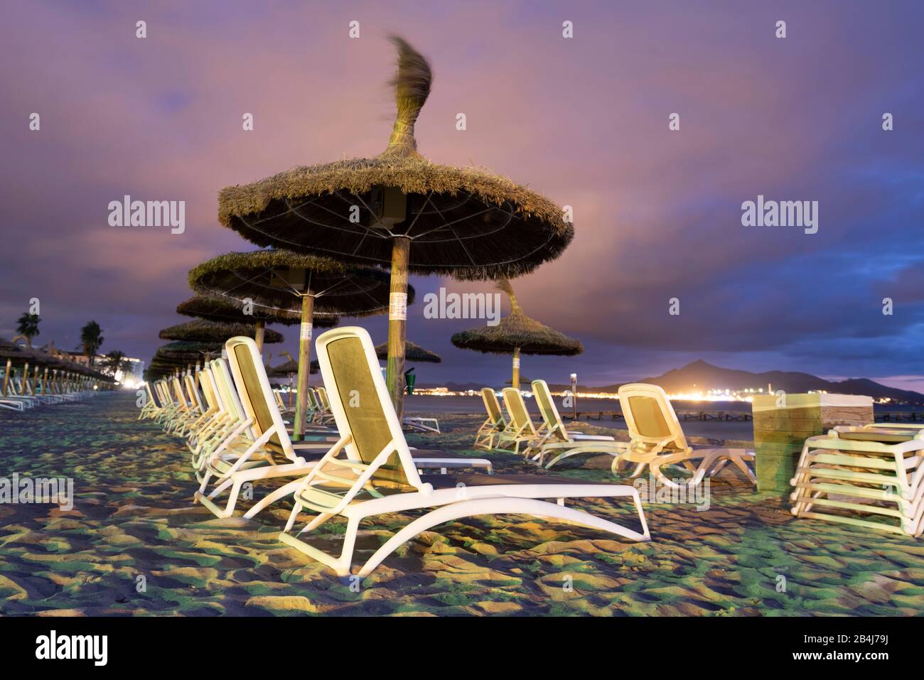 Spain, Mallorca, Playa de Muro, umbrellas and sun loungers on the beach Playa de Muro at the blue hour, north of Majorca. Stock Photo