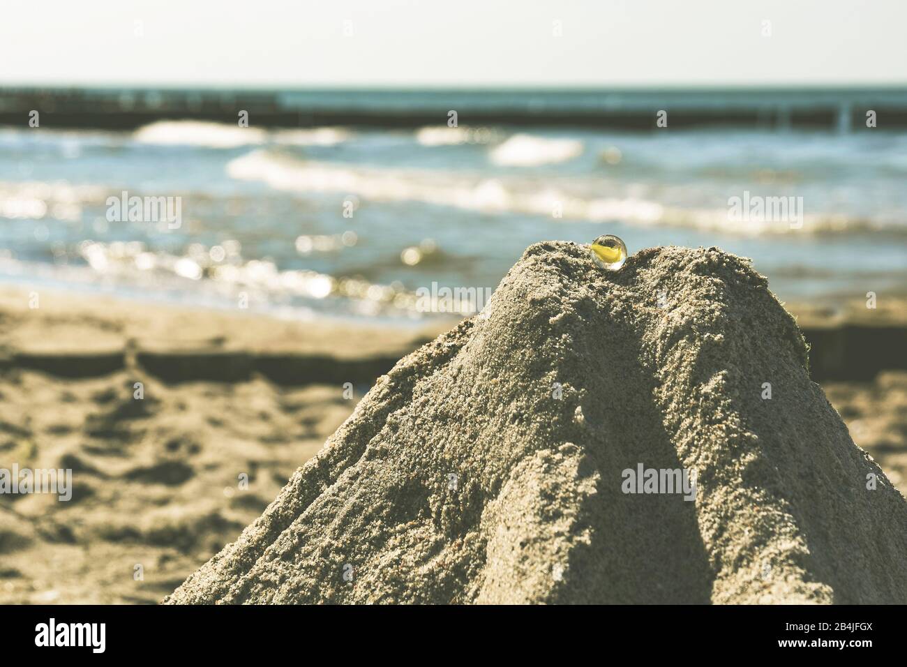 Close-up of sandcastle with glass marbles on the beach of the Baltic Sea, the sea in blur in the background Stock Photo