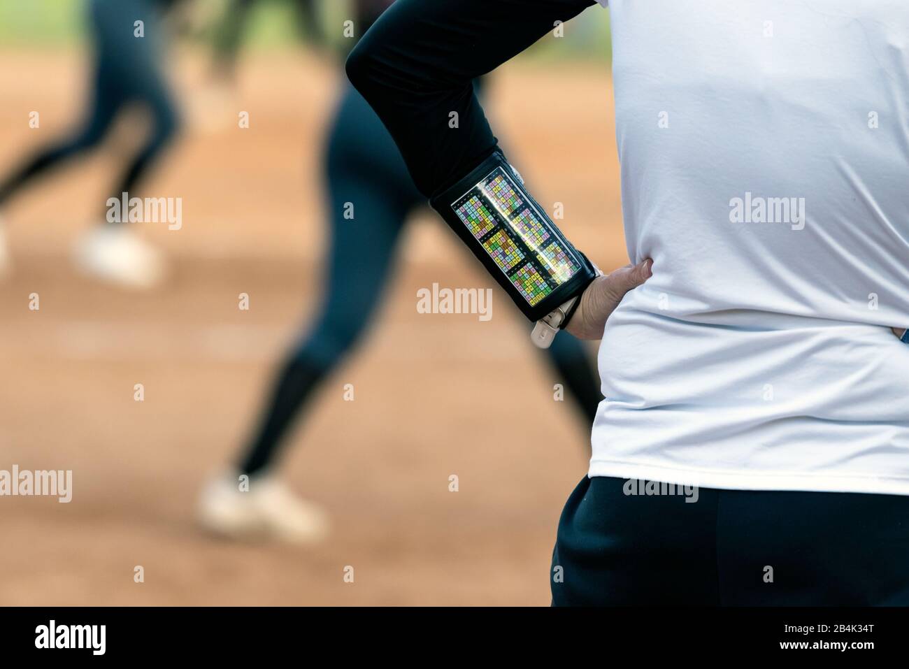 Third base coach for fast pitch softball team wears strategic offensive play arm band with disguised coded numbers. Stock Photo