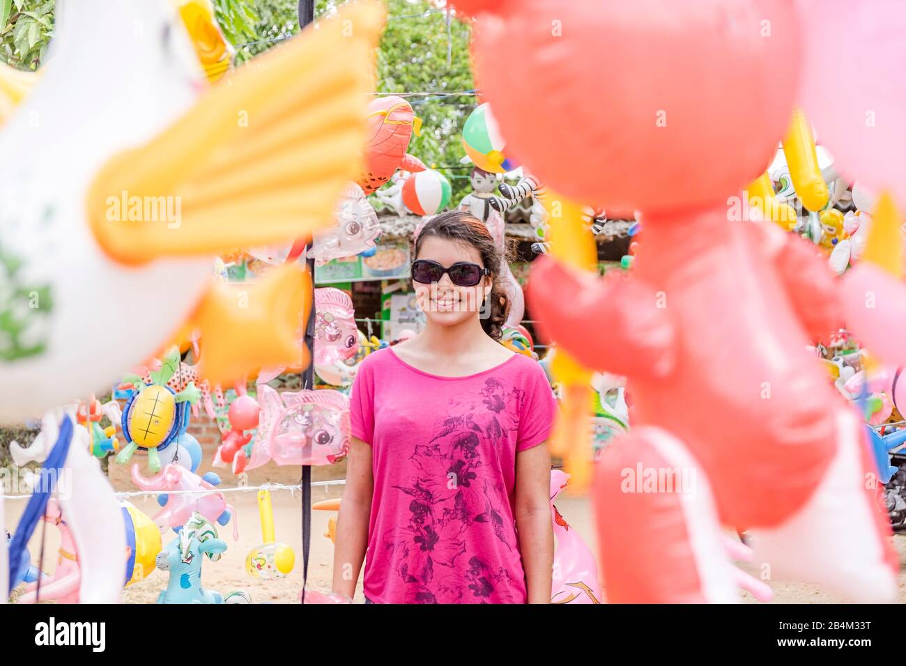 a young woman stands between gaudy colorful balloon animals Stock Photo