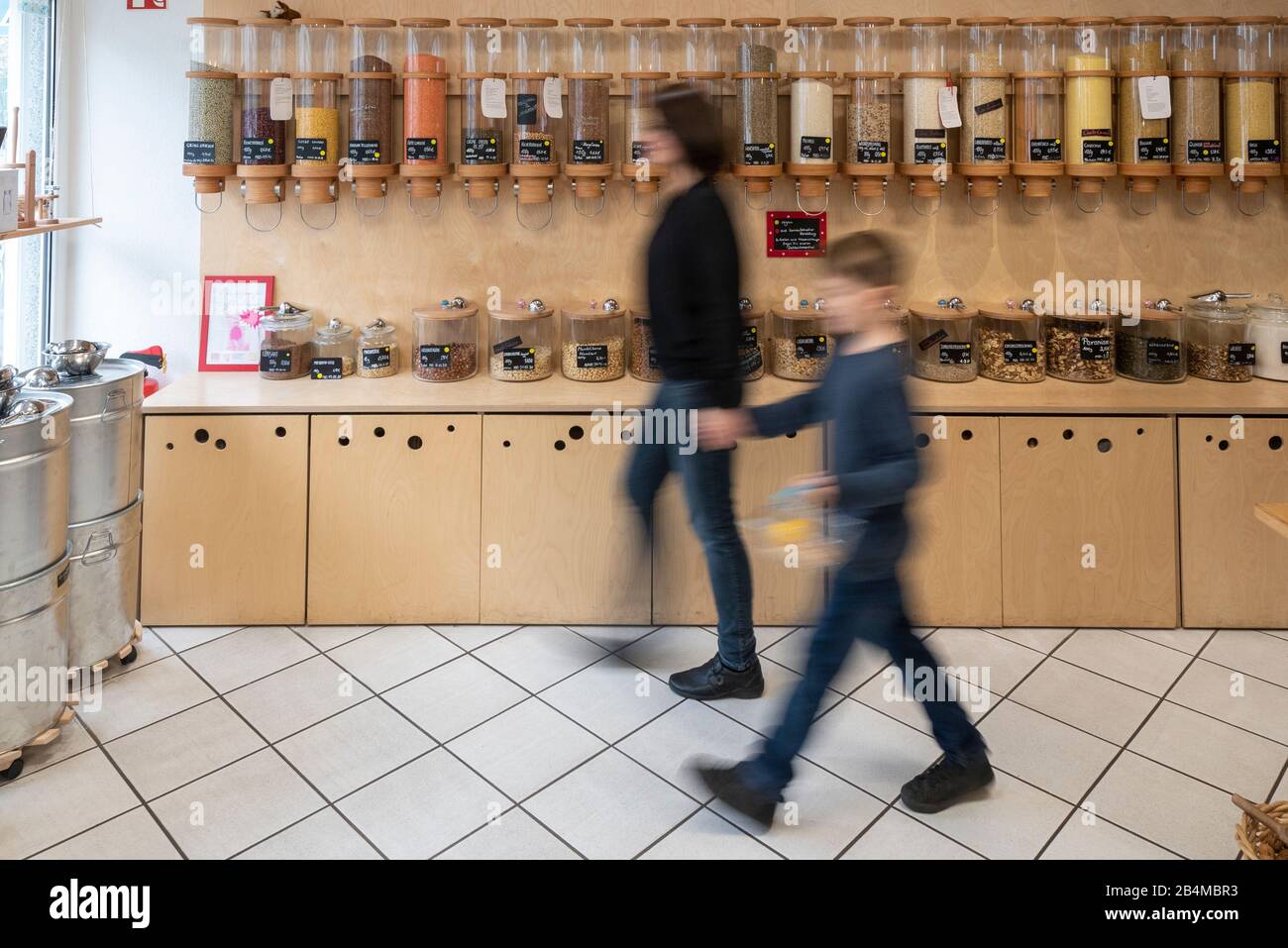 Eine Frau und ein Junge gehen an einem Regal mit Abfüllbehältern für Getreide vorbei, Szene aus einem Unverpacktladen. Stock Photo