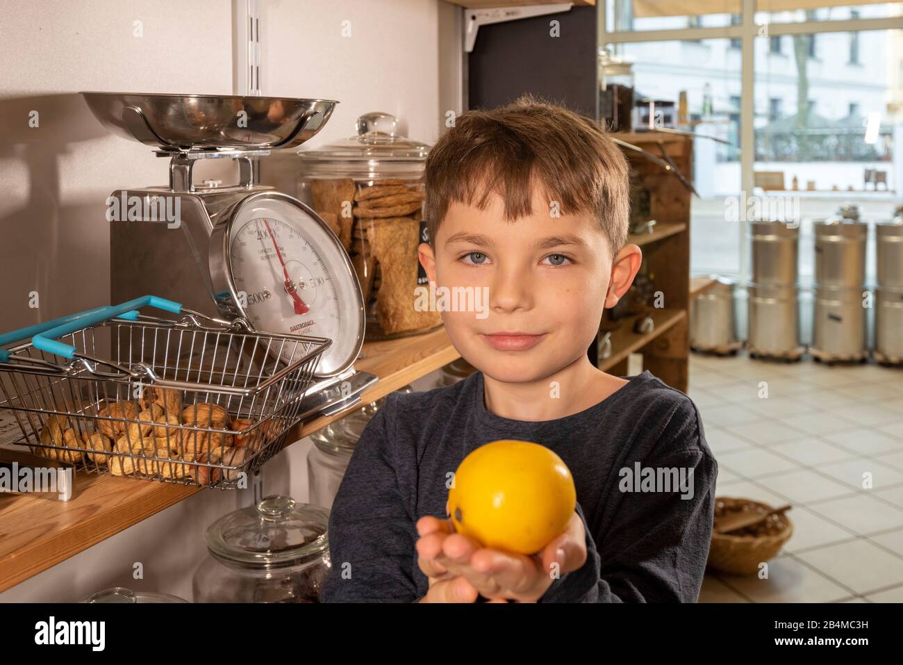 Eine Junge steht in einem Unverpacktladen an einer Waage. Er hält eine Zitrone in den Händen. Stock Photo