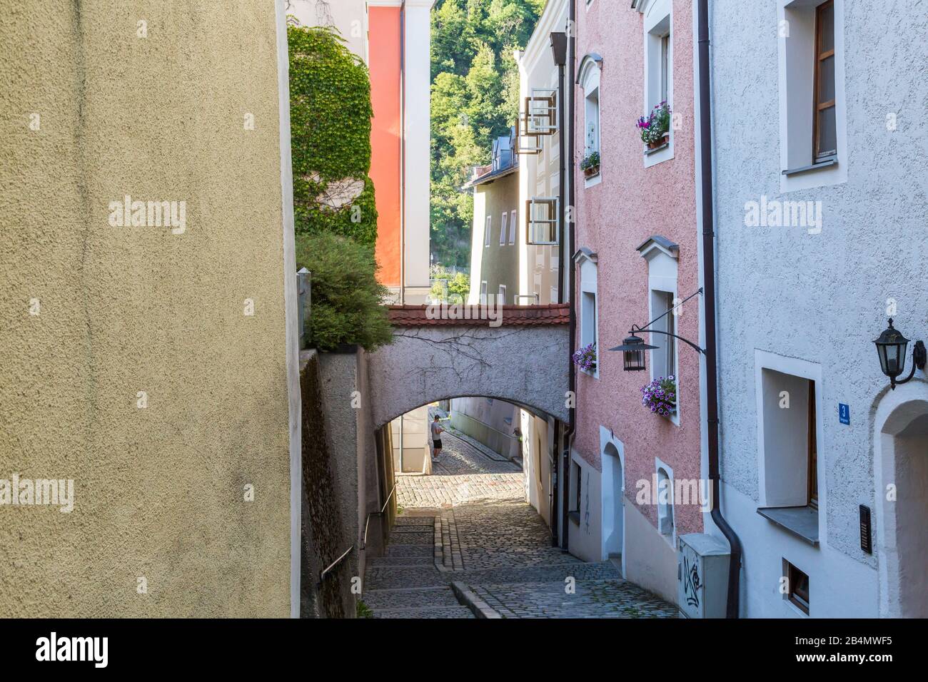 Quaint narrow cobbled lane in Passau, Bavaria, Germany in summer with arch between the buildings and view to trees Stock Photo