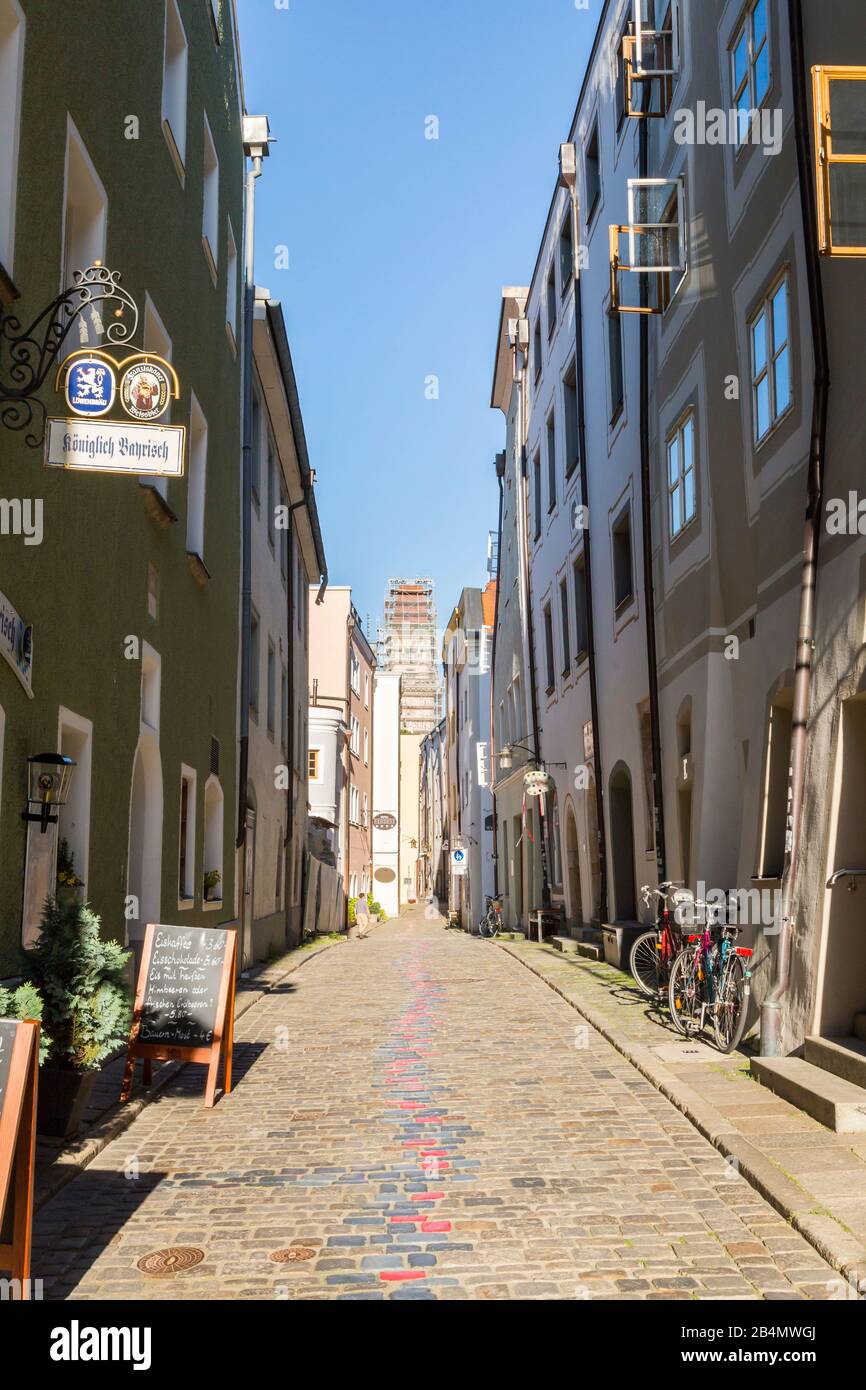 Quaint narrow cobbled lane in Passau, Bavaria, Germany in summer with arch between the buildings and view to trees Stock Photo