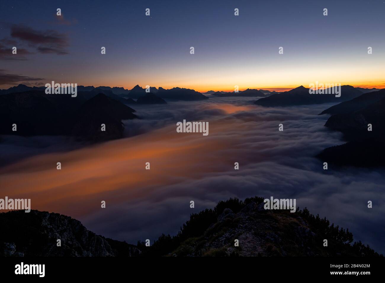 The lights of Maurach and Pertisau on Lake Achensee shine through under the sea of clouds of the rising high fog during a long-term night exposure. In the background the Karwendel Mountains, taken from the Ebener Joch in the Rofan. Stock Photo