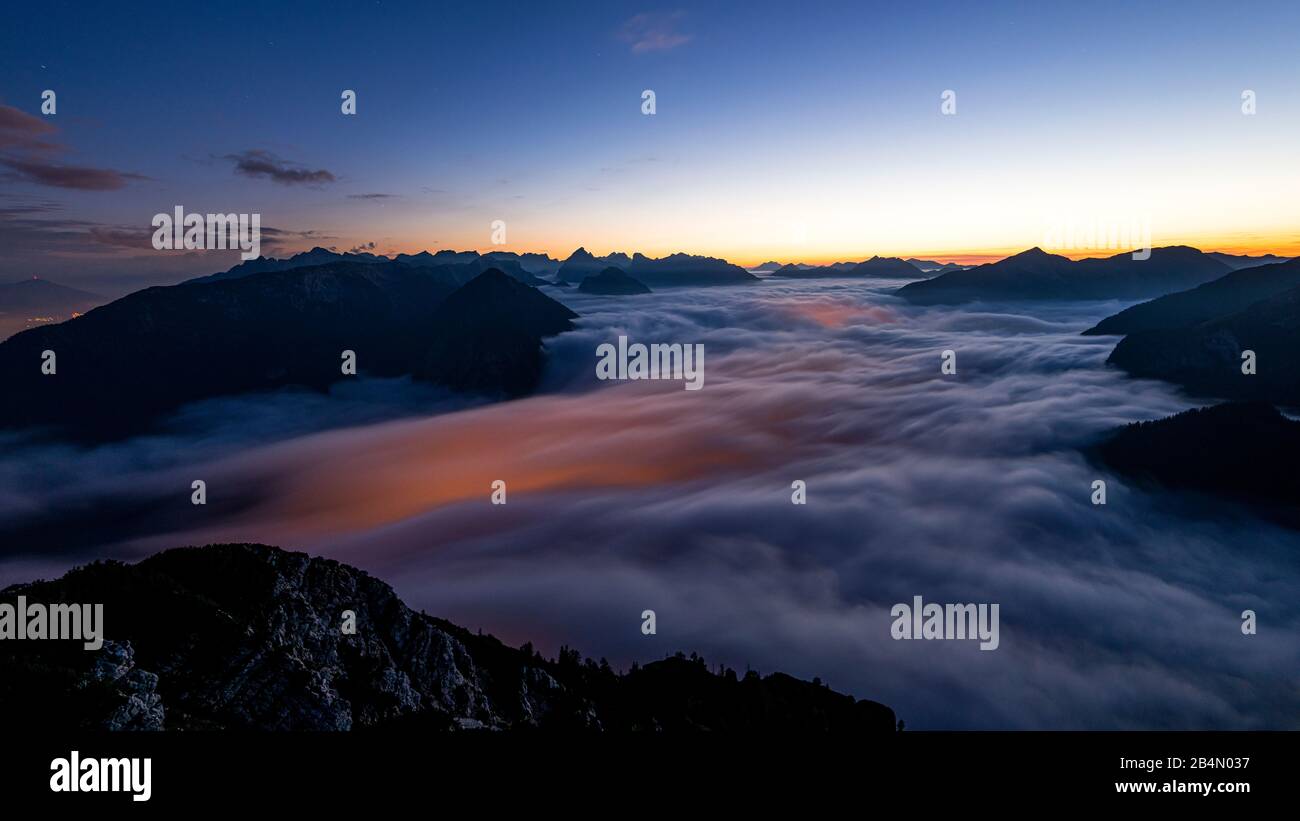 The lights of Maurach and Pertisau on Lake Achensee shine through under the sea of clouds of the rising high fog during a long-term night exposure. In the background the Karwendel Mountains, taken from the Ebener Joch in the Rofan. Stock Photo