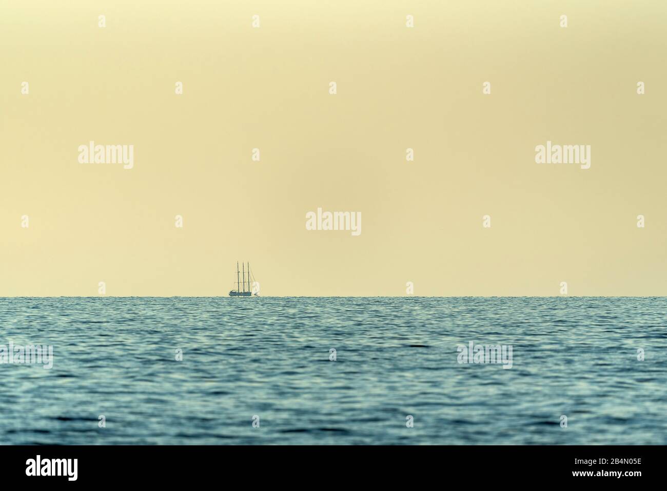 A sailing ship with three masts on the horizon in the Mediterranean. Slight waves in the foreground. Stock Photo