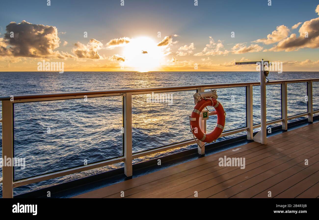 Sunset on cruise vacation. Sun just above the horizon and promenade deck with railing in the front. Stock Photo