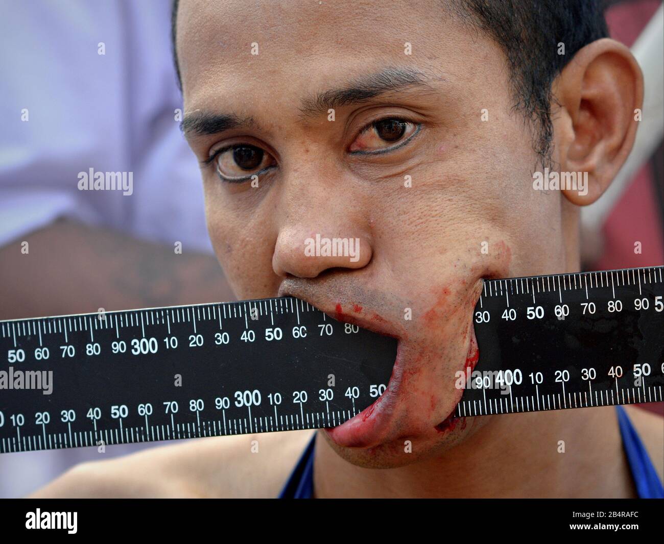 Young Thai Chinese Taoist devotee pierces his left cheek with a black metal ruler during the Phuket Vegetarian Festival (Nine Emperor Gods Festival). Stock Photo