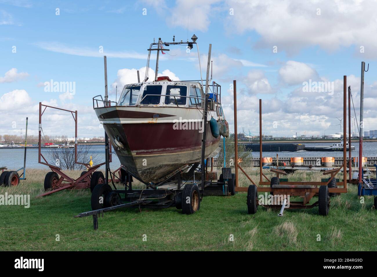 Old boat waiting on the dock on a trailer for restoration, in the background the port of Antwerp Stock Photo