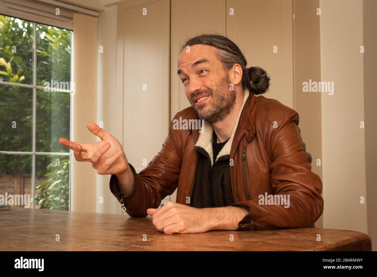 A man with a ponytail and a beard in conversation with someone Stock Photo
