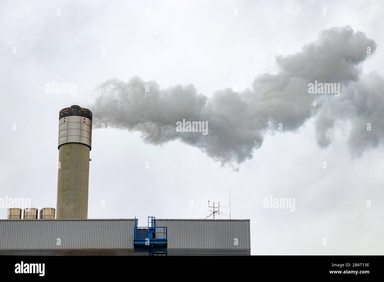 Powerplant with a chimney emitting gases into the atmosphere, causing air pollution. Gray, cloudy sky. Stock Photo