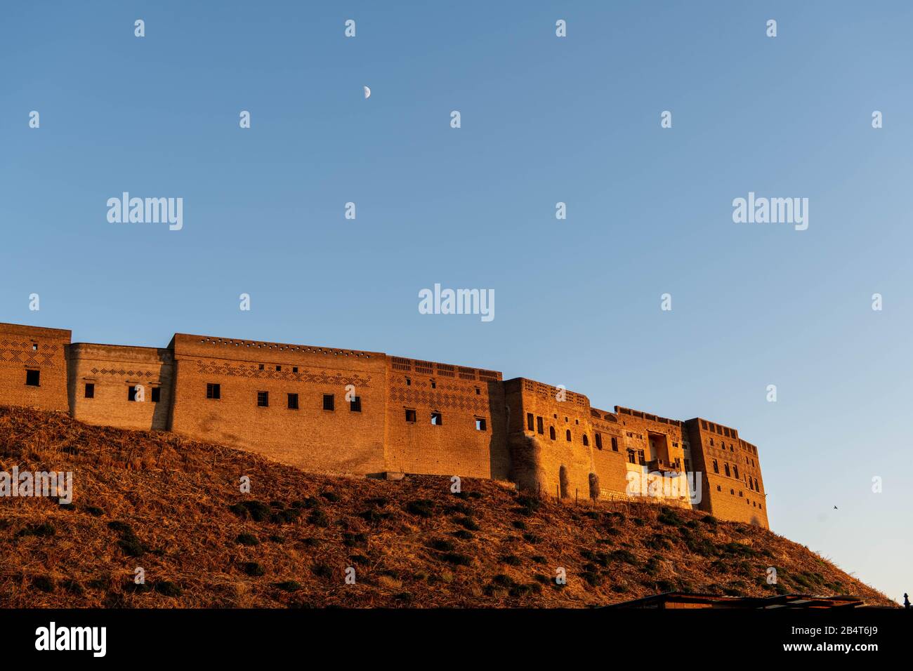Iraq, Iraqi Kurdistan, Arbil, Erbil. View of the Qalat citadel at sunset. Birds are flying in the background and the moon is shining. Stock Photo