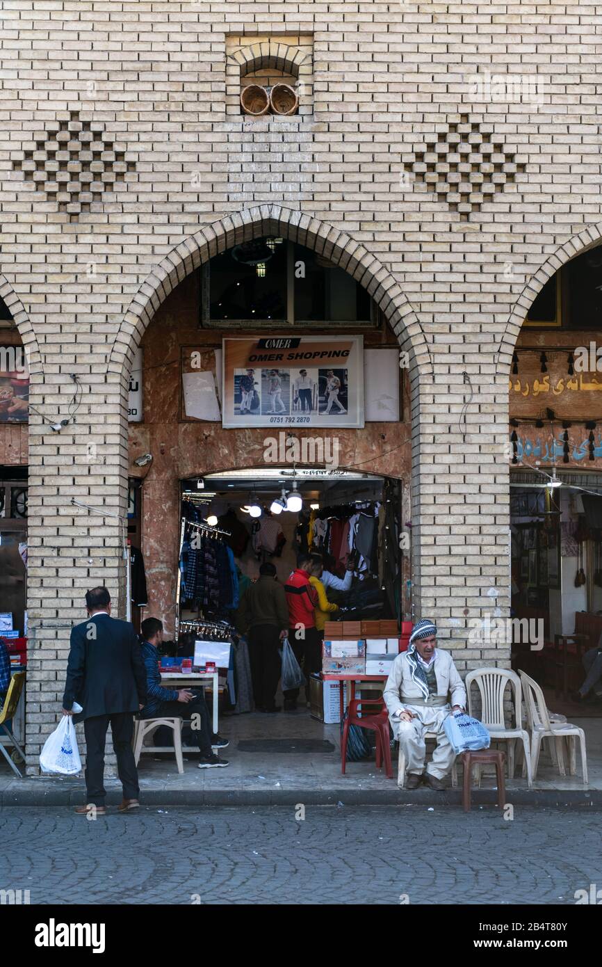 Iraq, Iraqi Kurdistan, Arbil, Erbil. Next to the entrance of the bazaar two men are sitting down next to the street under an arch drinking tea. Stock Photo